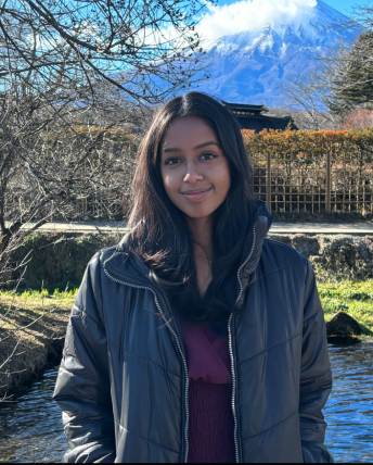 Anusha smiles outdoors in front of a small pond.