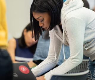 Side view of student standing and leaning over to type on a keyboard.