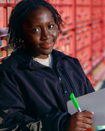 Tomi Babalola sits with a notebook and pen on a red metal bridge that crosses the Chicago river